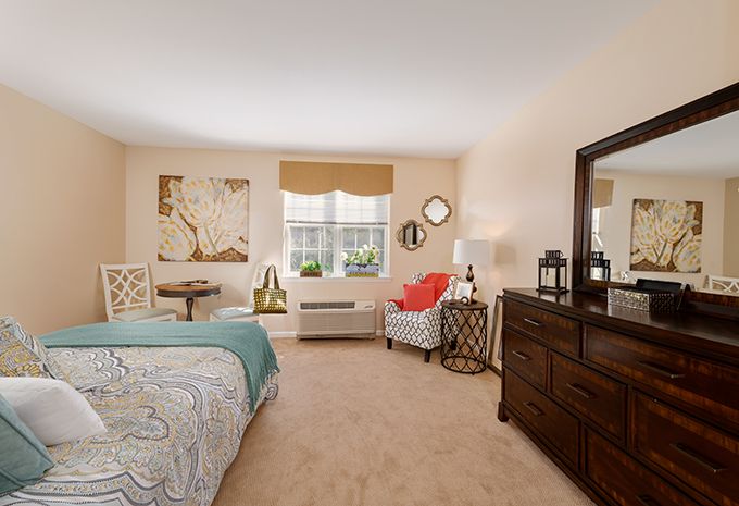 A cozy bedroom interior with a bed, dresser, chair, and various decor items.