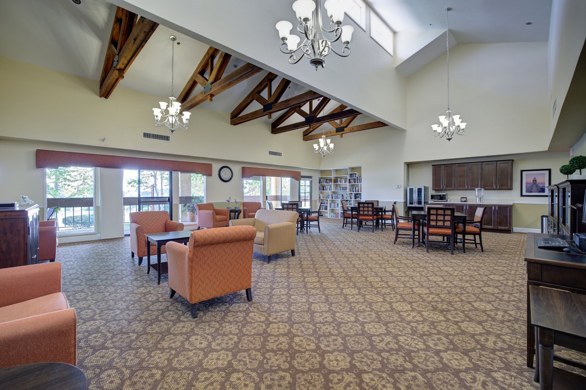 A spacious room with high ceilings and wooden beams, featuring a dining and seating area with elegant chandeliers.