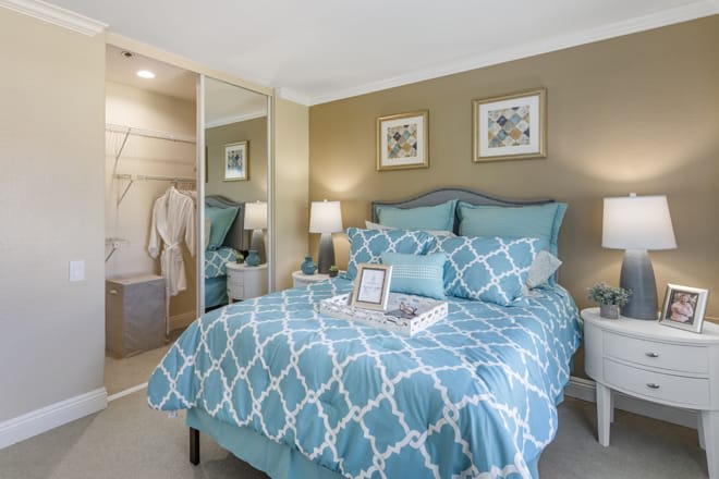 A cozy bedroom with a blue patterned bedspread, mirrored closet doors, and stylish decor.