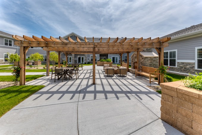 A spacious outdoor courtyard featuring a wooden pergola and patio furniture under a sunny sky.