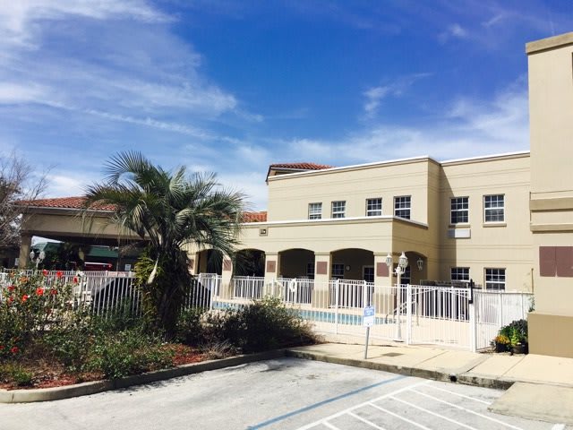 A school building with a palm tree and parking area under a clear blue sky.