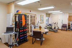 A physical therapy room with exercise equipment, including dumbbells and a stationary bike.