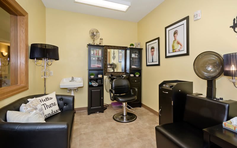 A cozy hair salon interior with a styling station, barber chair, and framed pictures on the walls.
