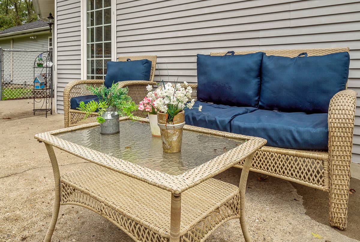 A cozy outdoor wicker patio set with blue cushions and a glass-topped table adorned with decorative plants.
