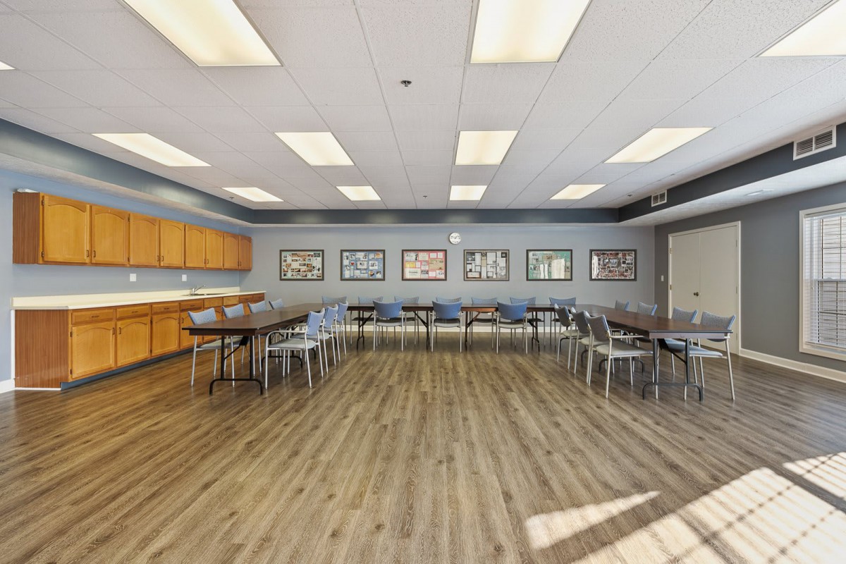 A spacious conference room with tables and chairs arranged for a meeting, featuring artwork on the walls and a wooden floor.