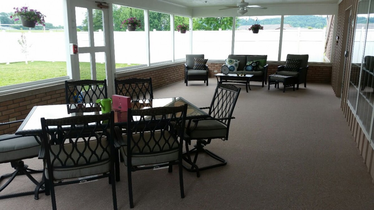 A cozy outdoor patio area with seating and tables surrounded by large windows.
