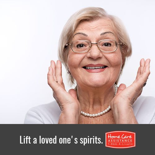 An elderly woman with glasses and a pearl necklace smiles warmly, lifting her hands in joy.