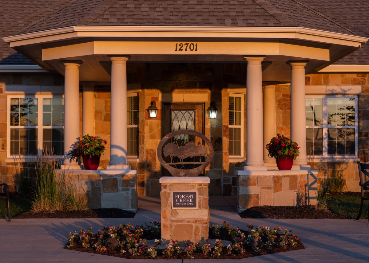 A charming house with a welcoming front porch, featuring pillars and neatly arranged landscaping.