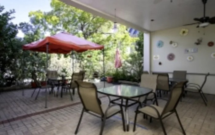 A cozy patio with a table, chairs, and an umbrella, surrounded by lush greenery.