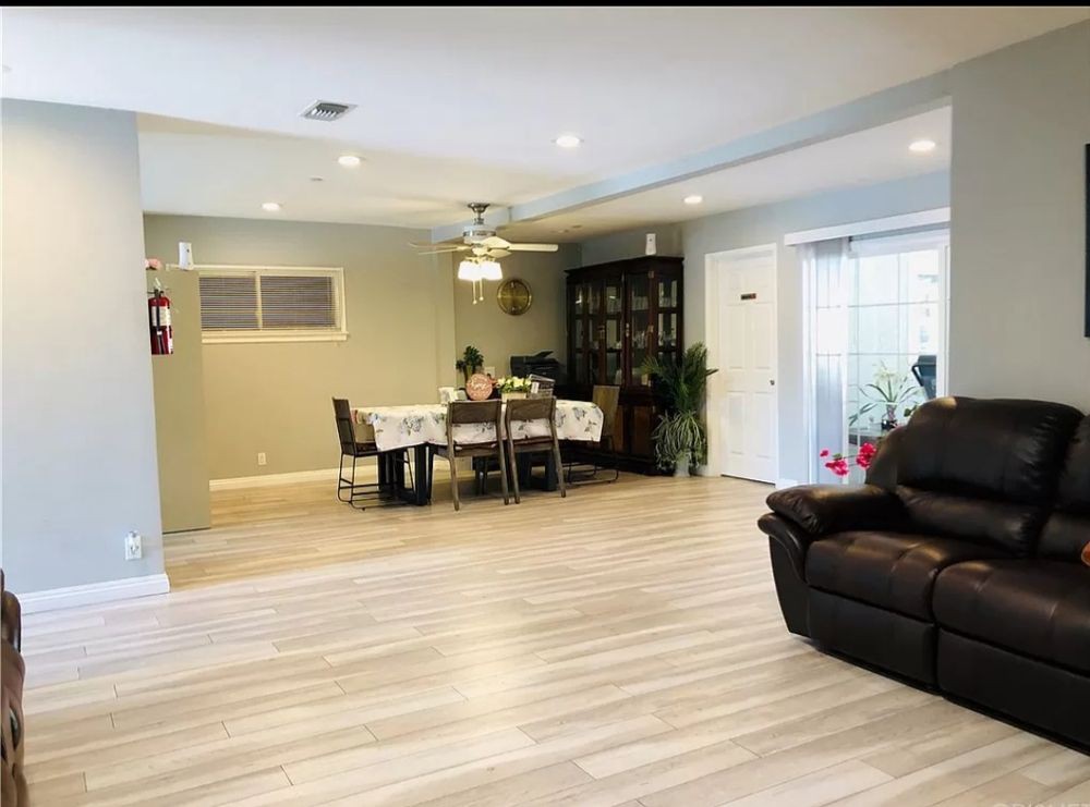A modern living and dining area with hardwood floors, featuring a ceiling fan and indoor plants.