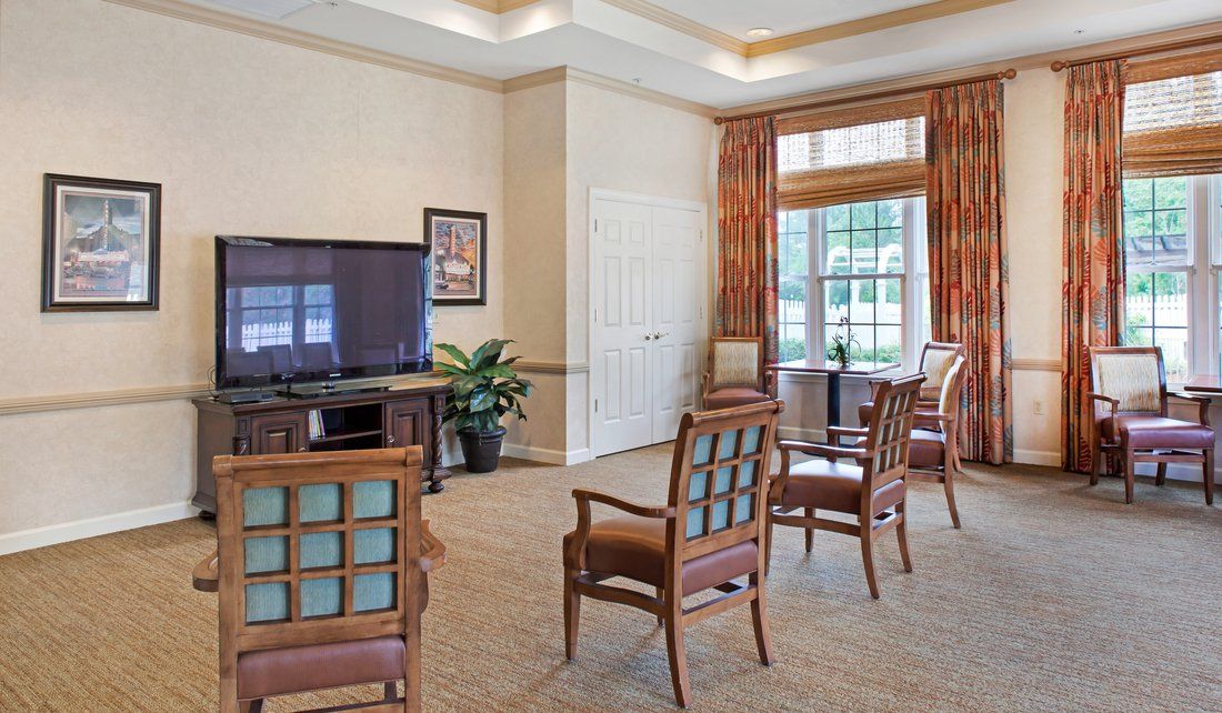 A well-lit living room area with chairs arranged in front of a television and a window with curtains.
