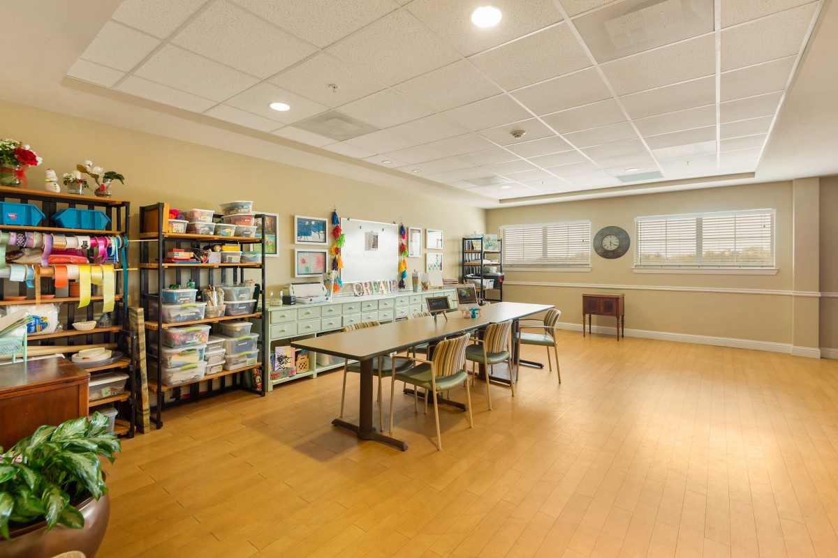 An empty classroom with tables, chairs, and shelves filled with art supplies.