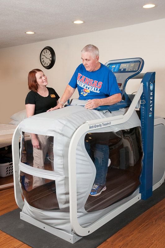 A person undergoing rehabilitation on an anti-gravity treadmill with a therapist providing guidance.