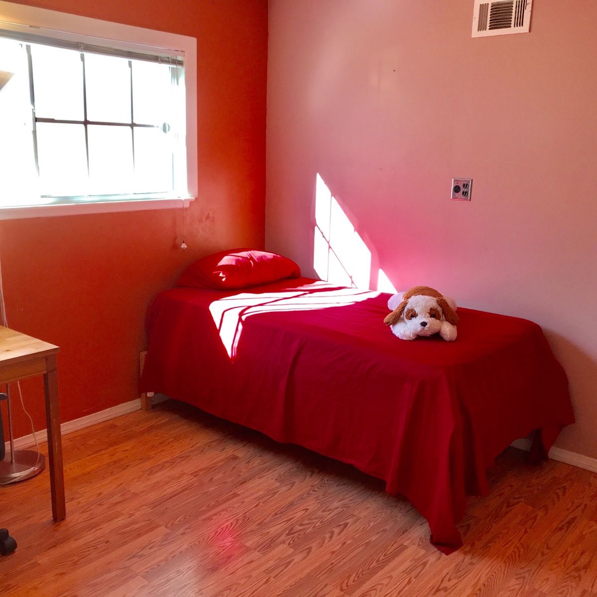 A bright bedroom with a single bed covered in red bedding and a stuffed animal on top.