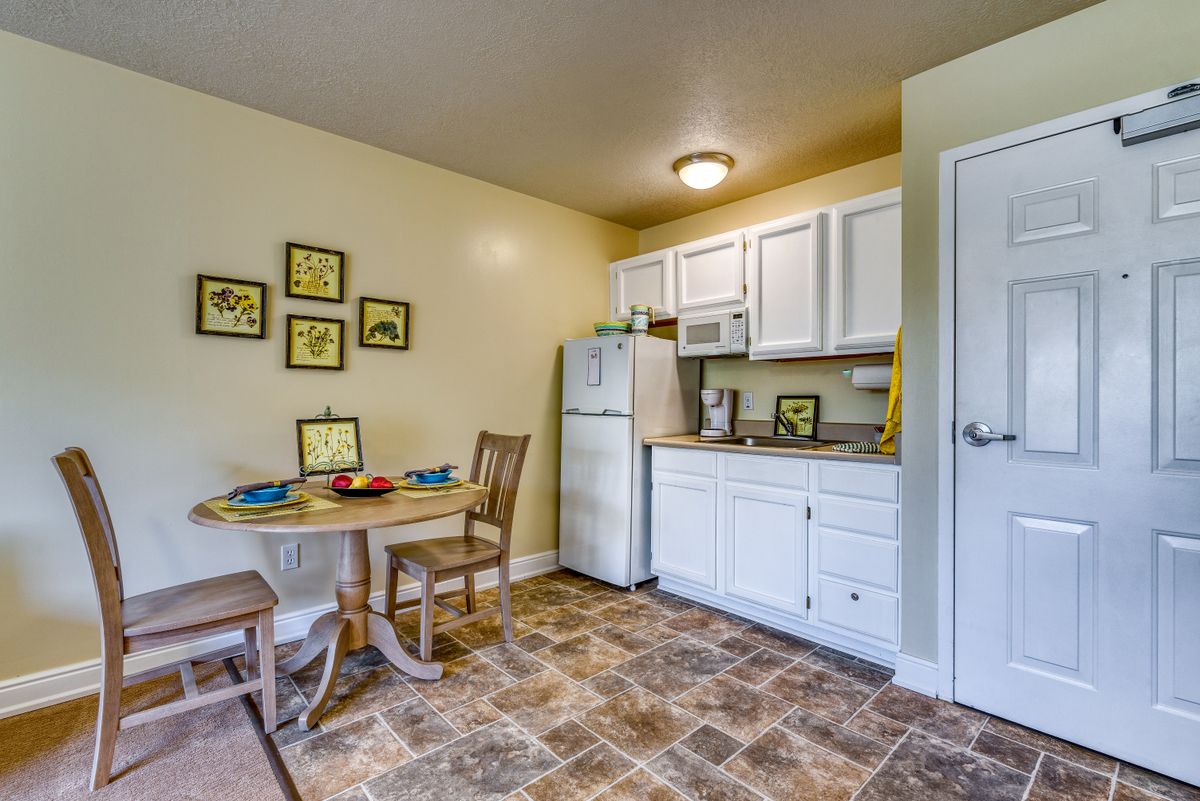 Cozy apartment kitchen with a small dining area featuring a table and chairs, white cabinets, and a refrigerator.