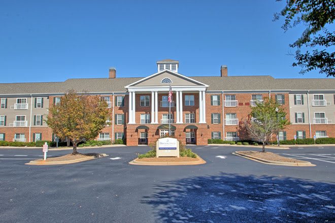 A symmetrical brick building with columns and a landscaped parking area.