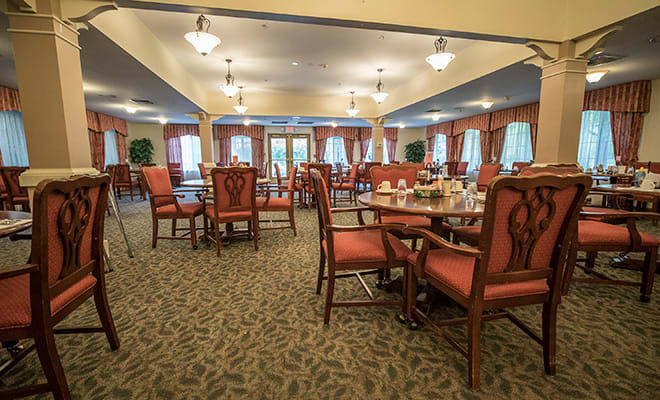 An elegant dining room with neatly arranged tables and chairs, decorated with warm lighting and curtains.