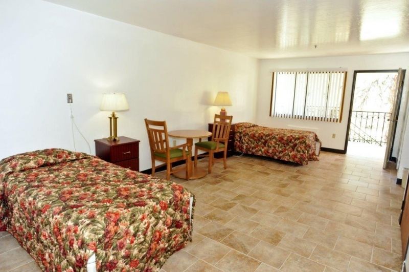 A spacious hotel room with two double beds, a small table with chairs, and lamps near the beds.