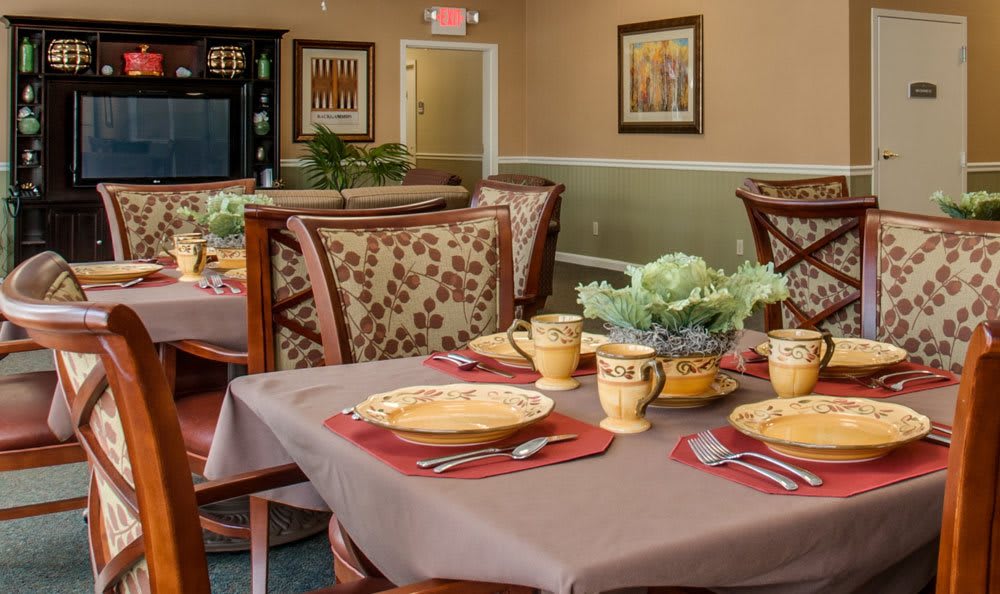 A warmly decorated dining room with set tables, featuring patterned chairs and elegant place settings.