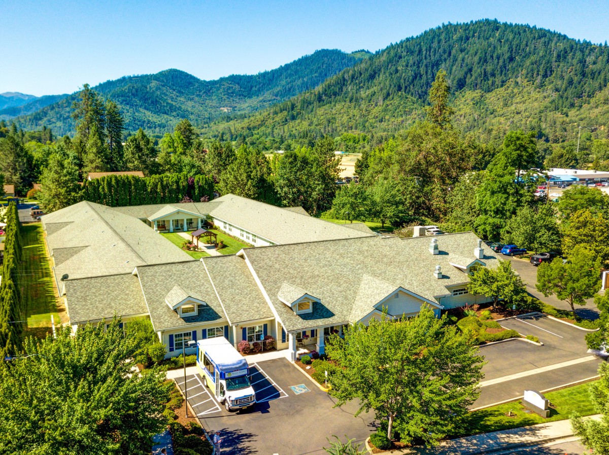 Aerial view of a building nestled in a lush, mountainous landscape with a parking lot and vehicles.