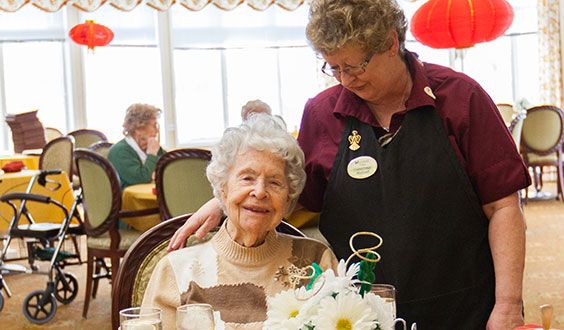An elderly woman celebrating her birthday with a cake and a caregiver beside her.