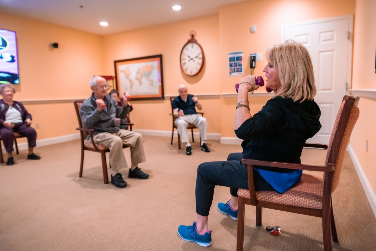 A group of seniors engaging in seated exercises in a brightly lit room.