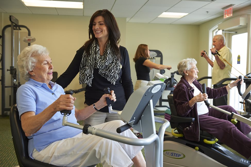 Seniors exercising in a gym with assistance from a trainer.