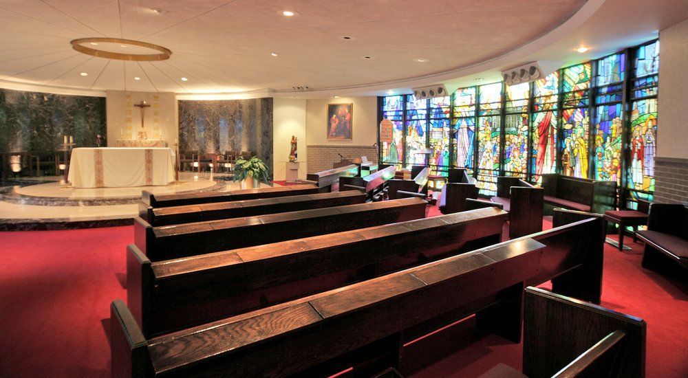 Interior view of a chapel with wooden pews and colorful stained glass windows.