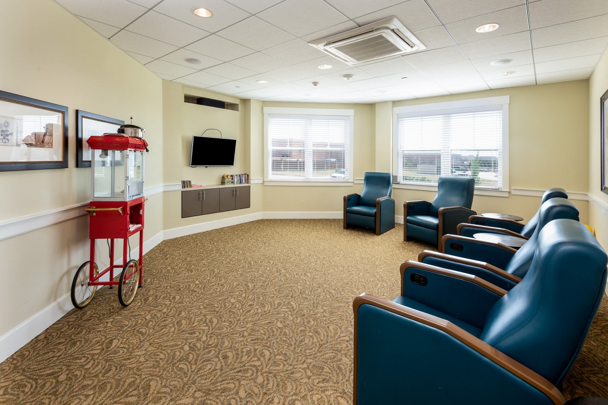 A cozy lounge area featuring comfortable chairs, a flat-screen television, and a popcorn machine next to large windows.