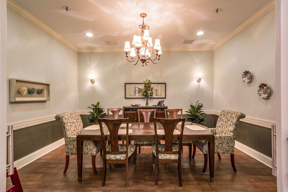 An elegantly decorated dining room featuring a large wooden table, surrounded by chairs and illuminated by a chandelier.