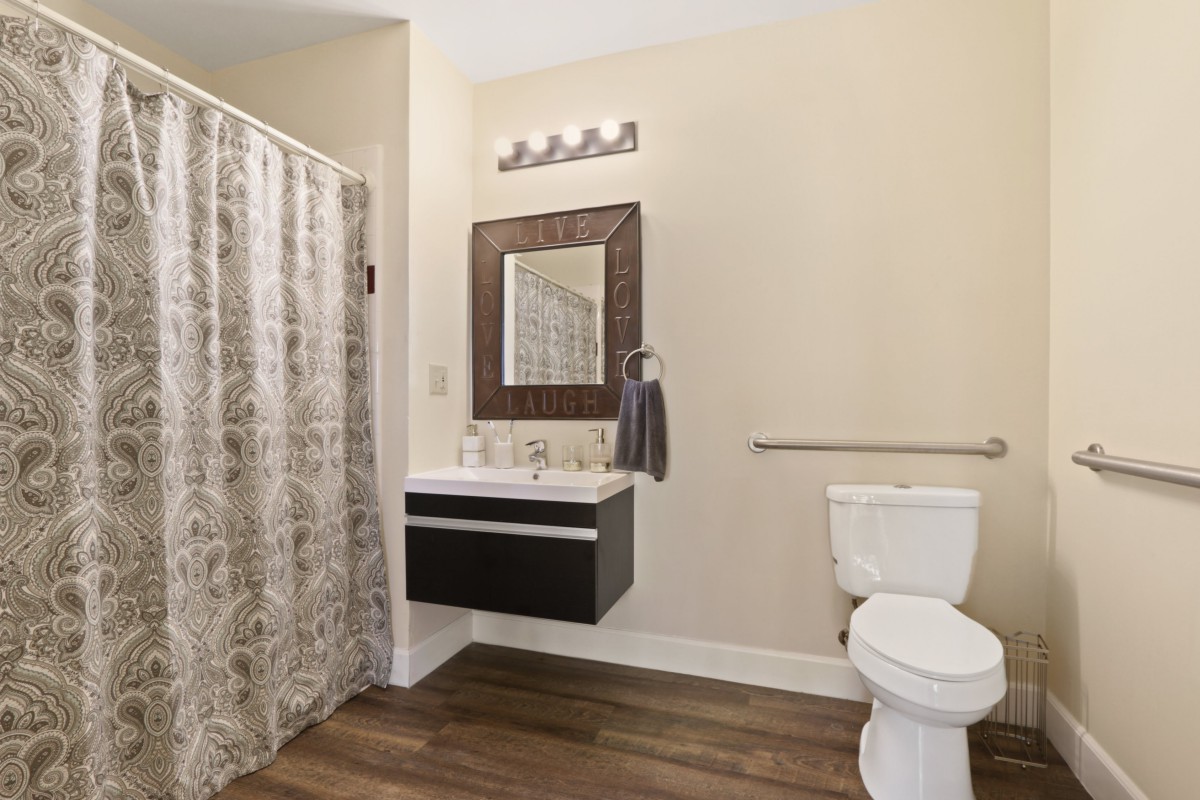 A modern bathroom with a wall-mounted vanity, large mirror, toilet, and shower with curtain.