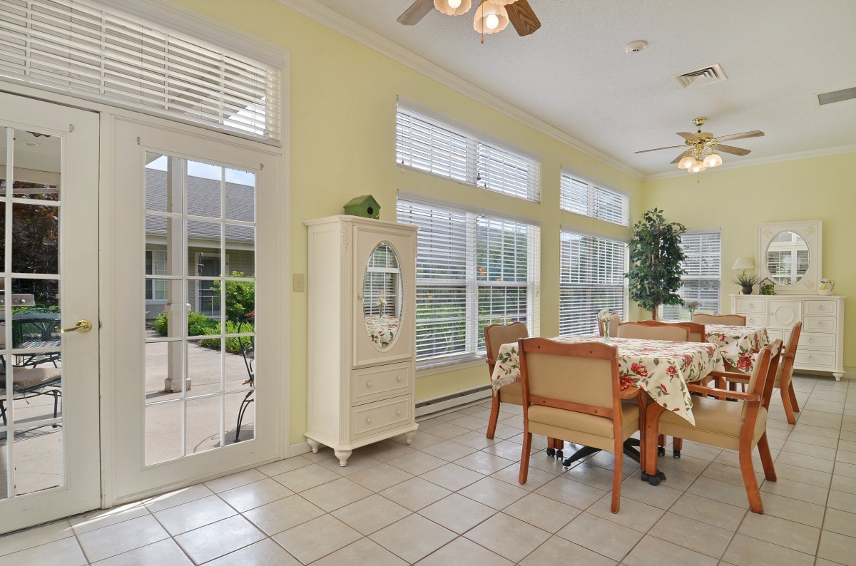 A bright dining area with large windows and glass doors, featuring a tile floor and natural lighting.