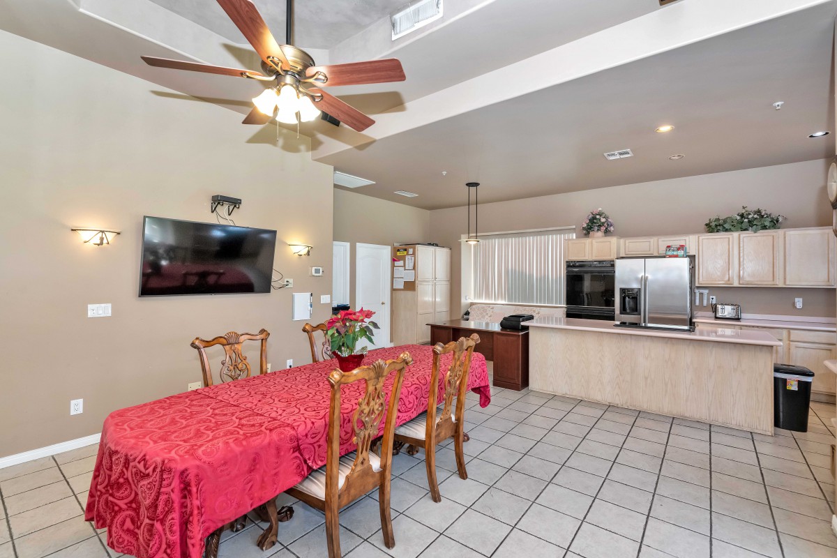 A spacious kitchen and dining area with a ceiling fan, featuring a large dining table draped with a red tablecloth.
