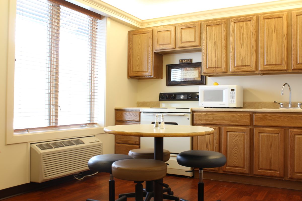 A cozy kitchen area with wooden cabinets, a round table and chairs, featuring a microwave and stove.