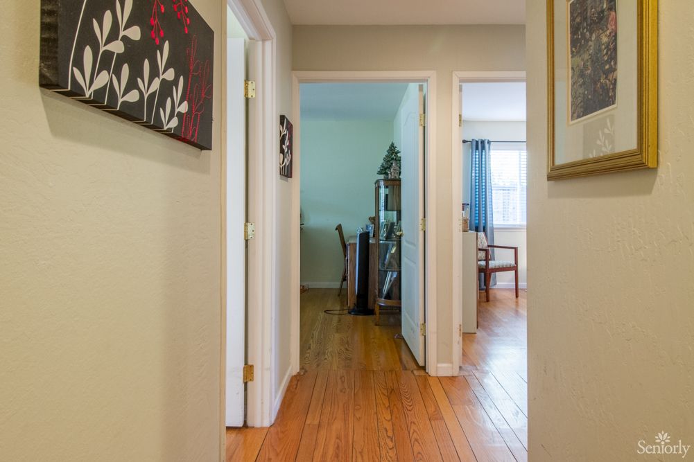A view down a well-lit hallway in a home, featuring wooden floors and multiple doors leading to adjacent rooms.