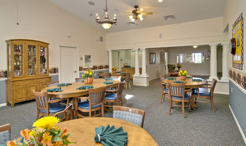 A dining room setup with multiple tables and chairs, decorated with flowers and napkins.