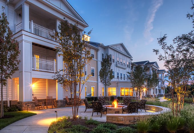 An evening view of a residential apartment complex with outdoor seating around a fire pit.