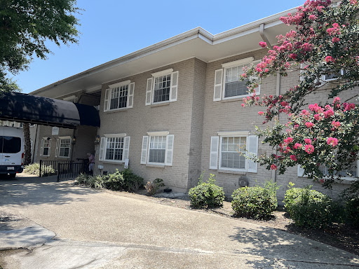 A two-story residential building with a gray exterior and blooming flowers in the foreground on a sunny day.