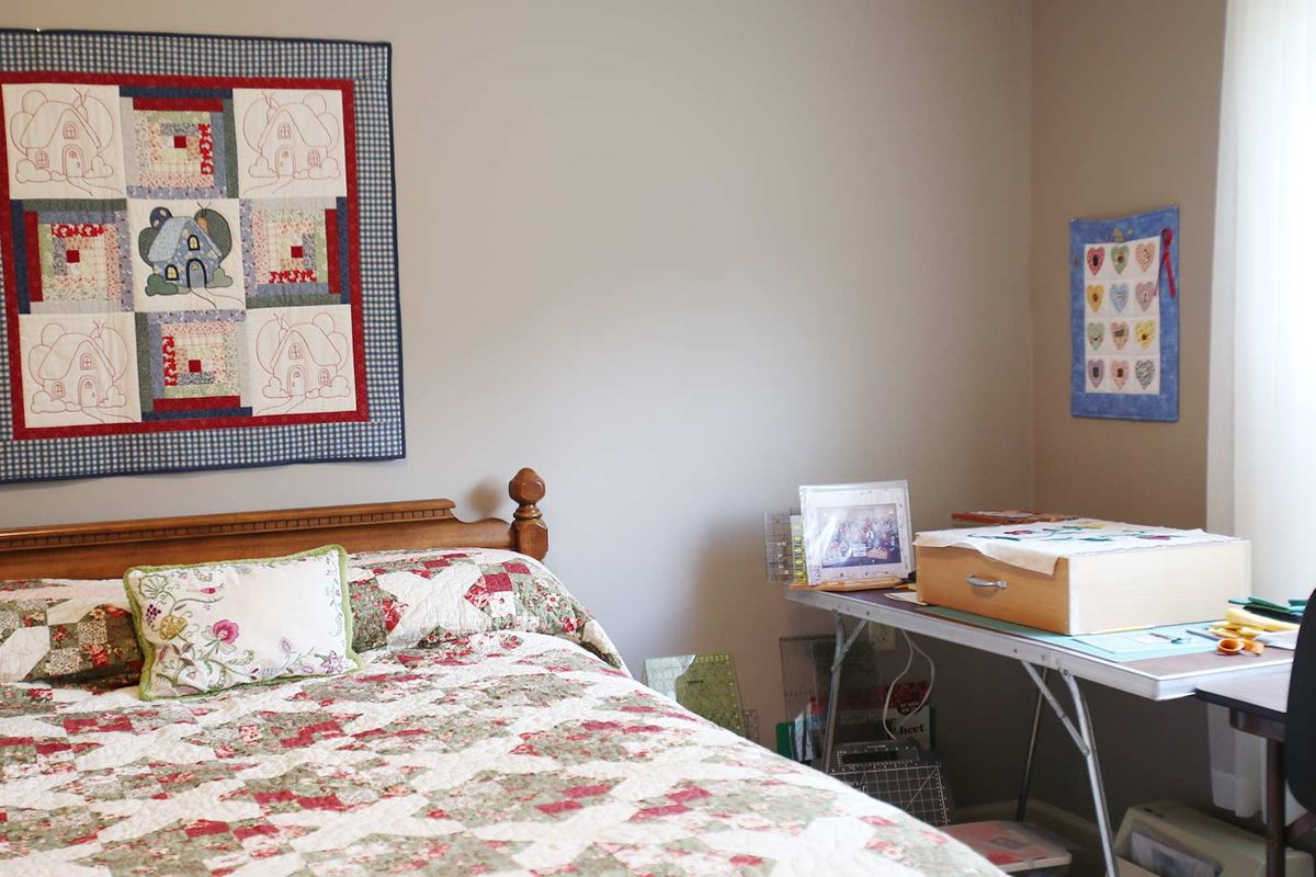 A cozy bedroom with a quilted bedspread and wall art, featuring a desk and lamp beside the bed.