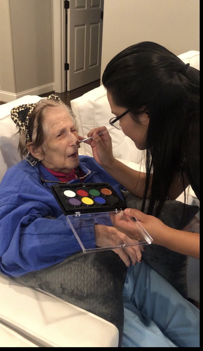 An artist applies face paint to an elderly person, highlighting a moment of creative expression and care.