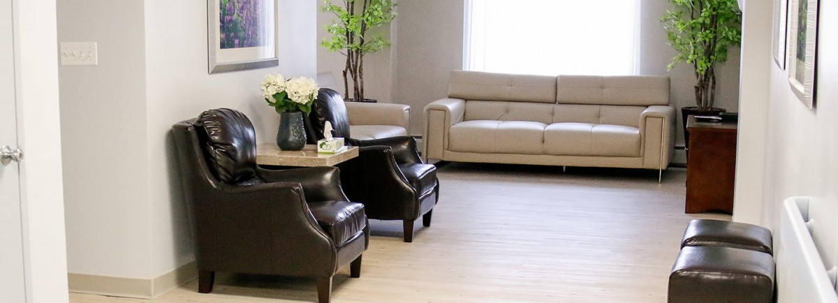 A modern living room with a beige sofa, two black chairs, and decorative plants.