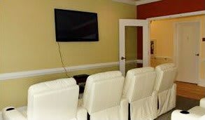 A cozy home theater setup with white seating and a large wall-mounted television.