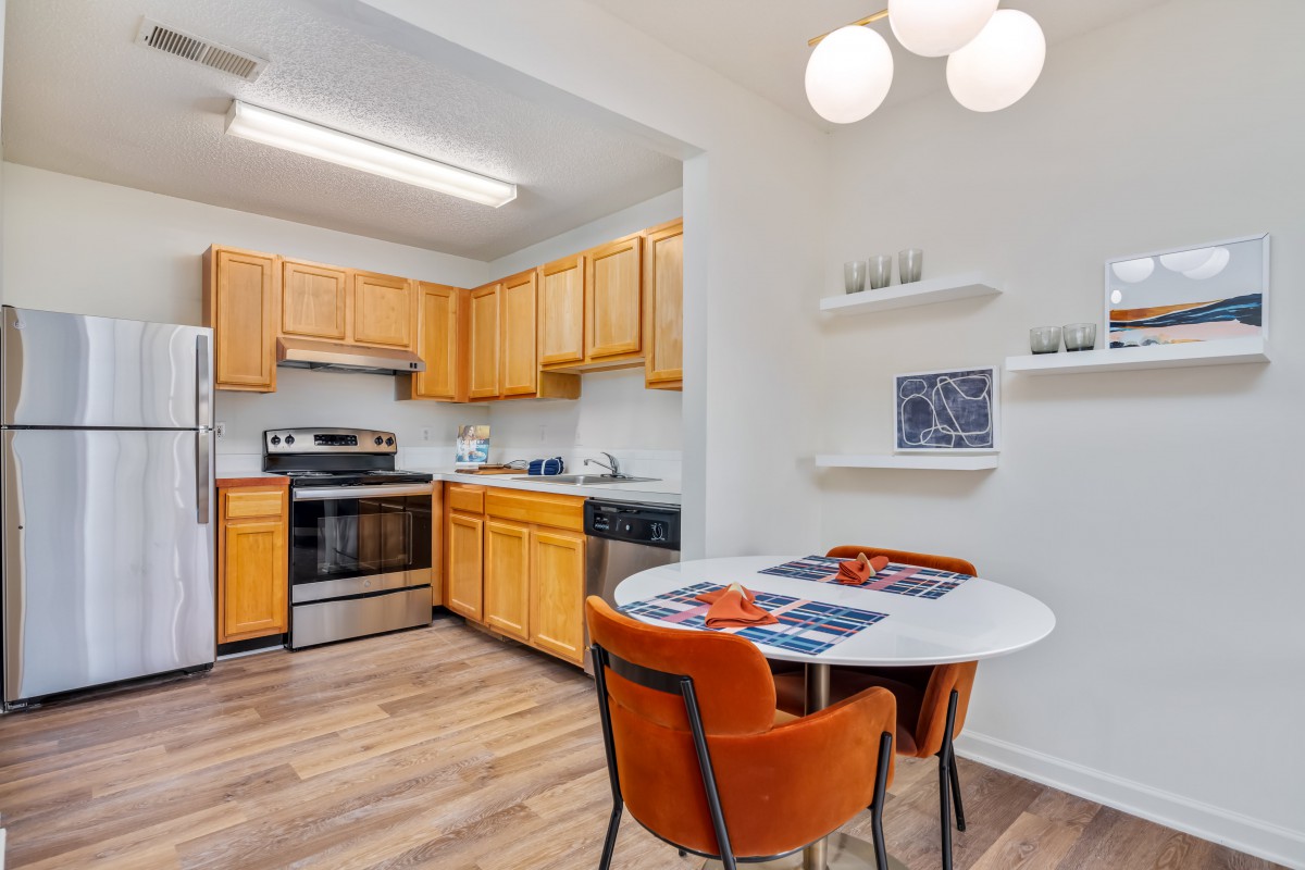 A cozy kitchen with wooden cabinets and a dining area featuring a round table and orange chairs.