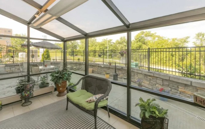A cozy sunroom with comfortable seating and lush plants, offering a serene view of the outdoors through glass walls.