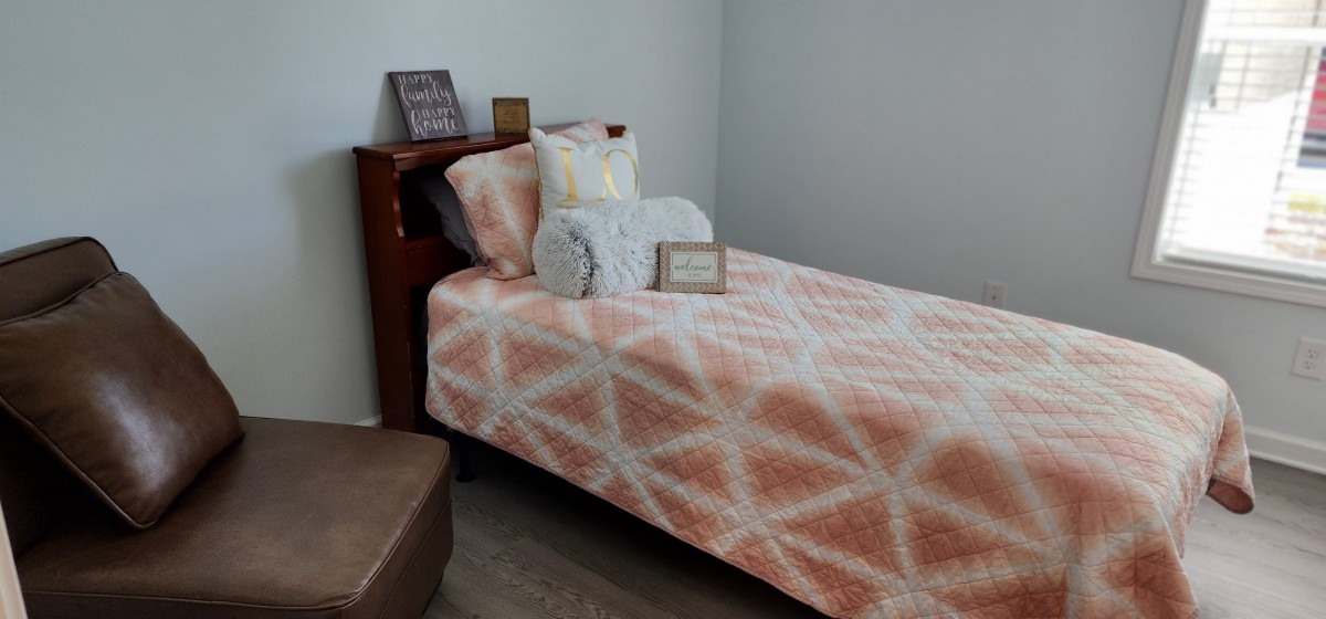 A cozy bedroom featuring a single bed with a geometric patterned quilt, adorned with decorative pillows and a wooden headboard.