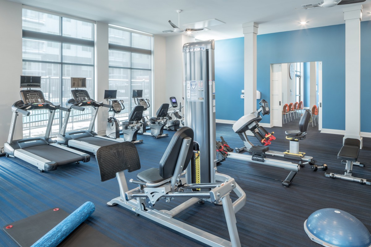 A modern gym with various exercise equipment, including treadmills, stationary bikes, and a weight machine.