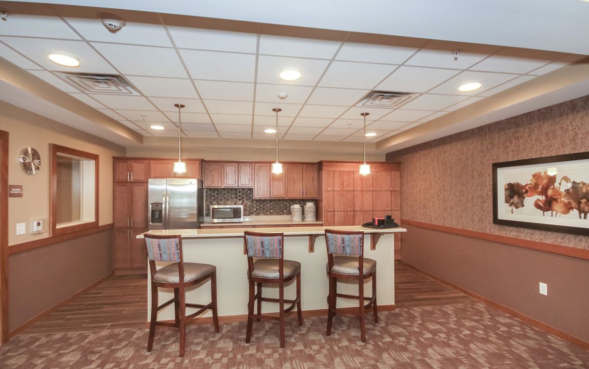 A spacious kitchen interior featuring a countertop with three bar stools and modern appliances.