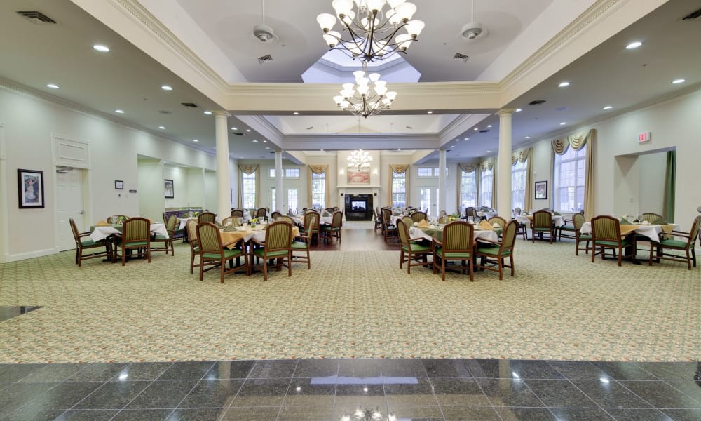 An elegant and spacious dining room with multiple tables, chandeliers, and a carpeted floor.