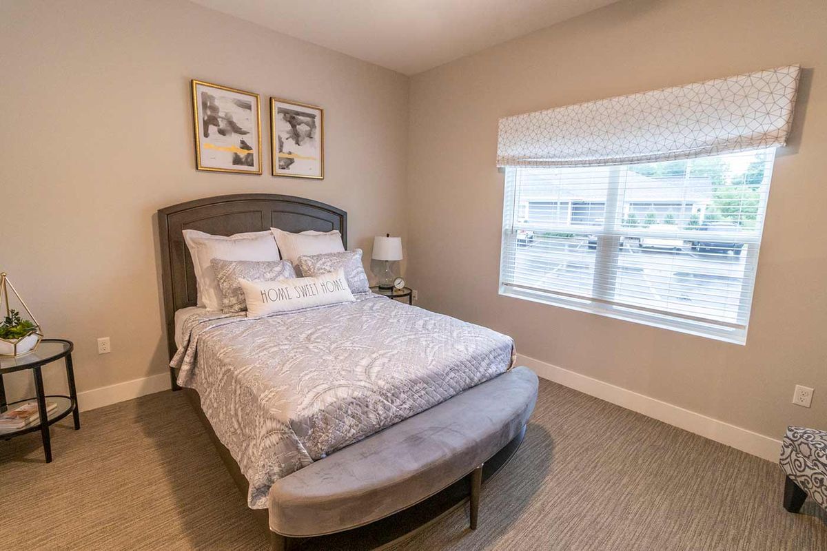 A cozy bedroom featuring a neatly made bed with decorative pillows, a bedside lamp, and a window allowing natural light.