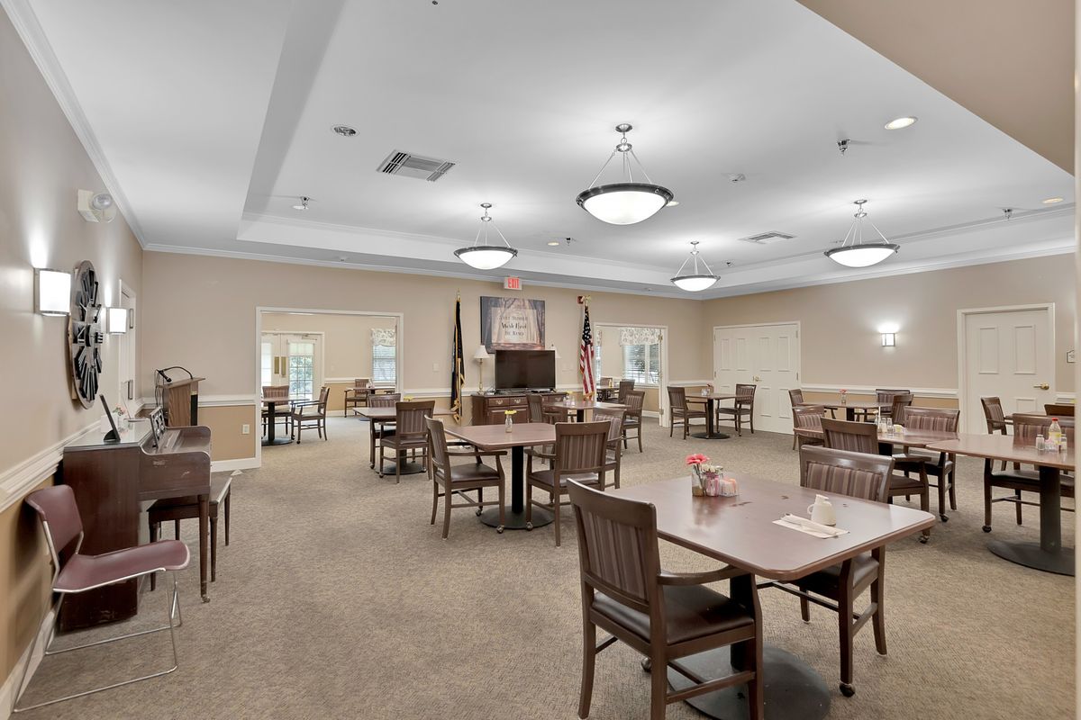 Spacious dining area with multiple tables and chairs, featuring overhead lighting and flags.